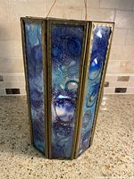 Full view of hexagonal brass framed candle lantern with iridescent, textured glass panels in blue, teal, and purple hues.