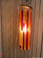 Side view of retro lucite hanging pendant lamp showing vertical colored rods and lighted glow.