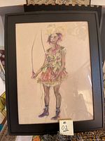 Framed original acrylic painting on paper showing a female figure in a colorful dress holding two sticks, photographed face on with reflections of light on the glass.