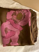 Folded scarf showcasing a large pink flower on a brown background to highlight the floral pattern and silk fabric texture.