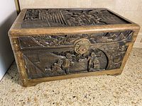 Front and top perspective showing carved figures, nature scenes, and brass closure, wood patina visible