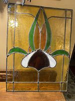 Front view of the stained glass panel showing the full floral design in green, white, amber, and textured amber glass with metal leading.