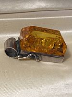 Side view of the amber stone set in sterling silver with curved decorative elements and the bolder bail.