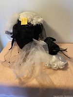 Four vintage ladies hats including black and white with veils, flowers, beads, and feathers arranged on a beige surface.