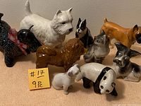 Nine miniature dog figurines including one panda figurine arranged on a beige surface with a yellow note indicating 9 pieces.
