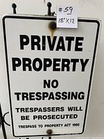 Full view of the metal private property sign showing black text on white background with rust marks around mounting holes.