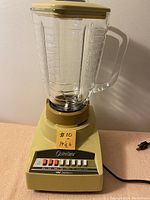 Front view of the vintage Osterizer blender showing the base, glass jar, lid, and control panel with speed buttons.
