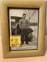Front view of the vintage 1943 black and white photograph within the beige textured Art Deco leather frame, showing a young man standing by a vintage car outdoors.