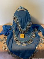 Blue sheer belly dancer's scarf displayed hanging and spread on flat surface, showing silver coins sewn along edge and turquoise crochet trim.