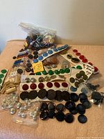 Collection of assorted vintage designer buttons laid out on a pink surface, showing a variety of colors, sizes, and shapes grouped by style and in plastic bags.
