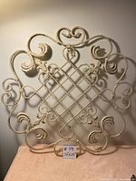 Full front view of vintage ornate rustic hanging wall decor showing symmetrical scroll and lattice design, cream distressed paint.