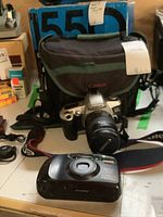 Pentax Espio 738 and Canon EOS with carrying bag and accessories shown on table.