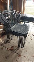 Four black metal outdoor chairs stacked together with padded seat cushions on a concrete floor