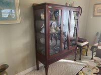 Front left angled view of wood china cabinet showing two glass doors, side panel, drawer and cabriole legs