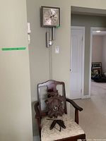 View of both clocks: cuckoo clock resting on chair with visible weights and pendulum clock hanging on wall.