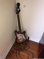 Full view of sunburst Saturn electric guitar leaning against wall with black cable coiled on floor