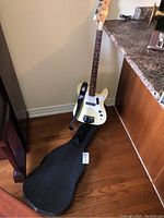 Full view of cream Yamaha bass guitar leaning against wall with soft case on floor