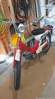 Front and right side view of red and white moped showing headlight, handlebars, seat and engine
