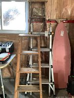 Overall view of two wooden step ladders in front of a wall, showing wear and condition.