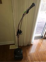 Full view of vintage Realistic microphone mounted on black adjustable height stand with weighted square base, placed on wooden floor near curtain and sliding glass door.