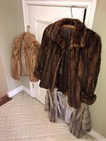 Three vintage ladies mink jackets hanging on door. Two light brown/cream colored, one dark brown with cream fur trim at bottom.