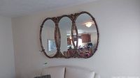Full view of the mirror showing its three connected oval glass panels and ornate frame hanging on a wall above a couch.