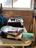 Full view of Akai reel to reel tape player and stack of vintage audio tapes and boxes on table below it.