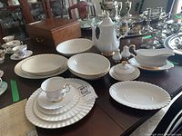 Overview of white bone china service and gold-trimmed pieces arranged on dining table alongside silver items