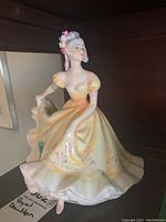 Front view of the Royal Doulton Ninette HN2379 figurine showing the detailed facial features and yellow dress with floral accents.