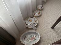 Four Royal Worcester Evesham china pieces lined up on carpet near window: three covered bowls with lids and one serving bowl. All have fruit and gold rim decorations.