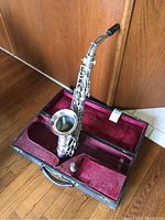 Full view of saxophone in open hard case showing body, neck and mouthpiece resting in red plush interior