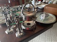 Set showing overall lot items including the hot water dispenser, candlesticks, wine goblets, and serving tray on a wooden table with other household items in background.