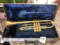 Vintage brass trumpet resting inside a black hard case lined with dark blue plush fabric, showing overall wear.
