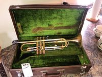 Vintage trumpet lying in an open hard case with green velvet lining.
