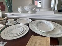 Full view of the set displayed on a mantle showing the serving dishes, soup bowl with lid, cups, saucers, plates and gravy boat.