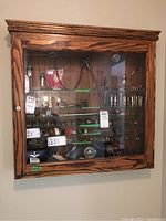 Front view of the oak wood display cabinet mounted on a wall, showing glass door with decorative molding and visible contents inside.