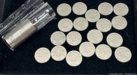 Full roll of 25 Canadian 5-cent coins in a plastic coin tube along with 25 coins spread out on black cloth background