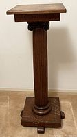 Full view of the antique carved oak plant stand showing its square top, column, and base with foot supports.