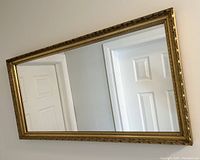 Full view of the large antique wall mirror showing the rectangular shape and ornate gold-toned frame reflecting white doors.