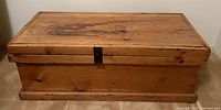 Front view of closed antique wooden blanket box showing wood finish, metal latch, and base.