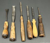 Six antique wood carving chisels laid flat showing wooden handles and metal blades of varying widths and shapes.