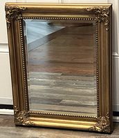 Full view of the ornate vintage bevelled glass mirror showing the entire gold-colored detailed frame and clear glass surface.