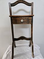 Front view of the antique wooden stand showing the full structure, drawer, and curved legs and handle.