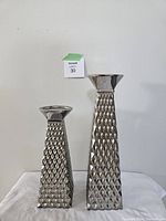 Front view of two silver painted pottery candle holders with diamond embossing, one taller and one smaller.