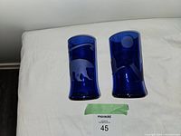 Two etched cobalt blue glasses showing bear and moon designs, placed on a white surface with measurement reference.
