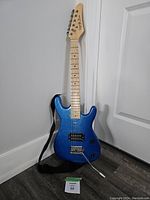 Full photo of right handed blue kids electric guitar standing upright with strap attached.
