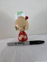 Japanese Kokeshi doll shown standing next to a black Sharpie marker for size comparison, under 3 inches tall.