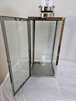 Metal and glass lantern with door open, showing interior and metal base