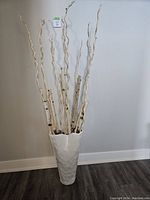 Front view of large white vase with birch branches and decorative sticks showing texture and height