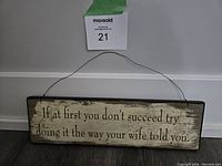 Photo of the metal sign leaning against a wall showing the entire sign and wire hanger.